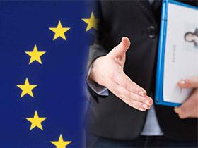 Osoba z wyciągnięta ręką do powitania i dokumentami w drugiej, w tle flaga Unii Europejskiej