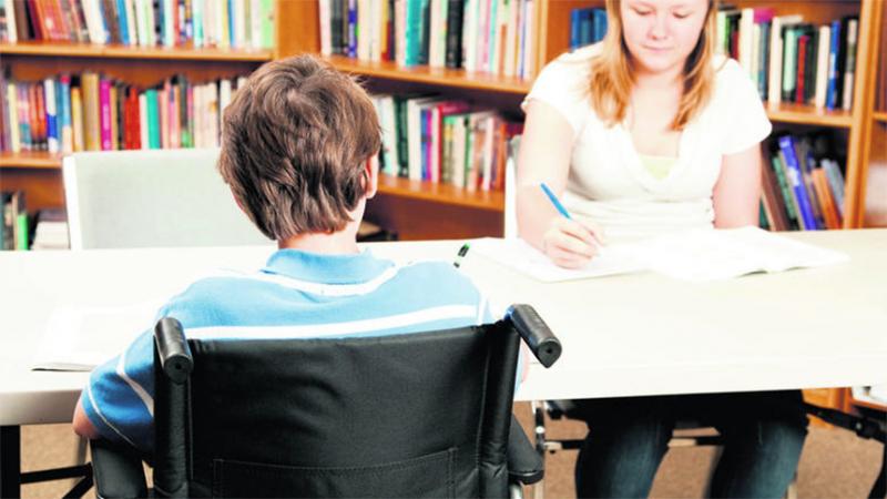 Chłopiec na wózku inwalidzkim siedzący w bibliotece na przeciw dziewczynki