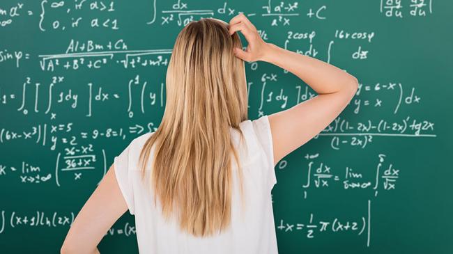 Młoda kobieta stoii przed tablicą zapisaną równaniami matematycznymi