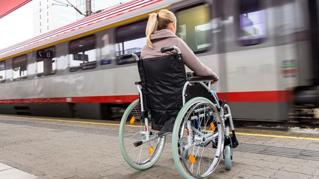 Kobieta na wózku inwalidzkim na preonie, w tle przejrzdzający pociąg