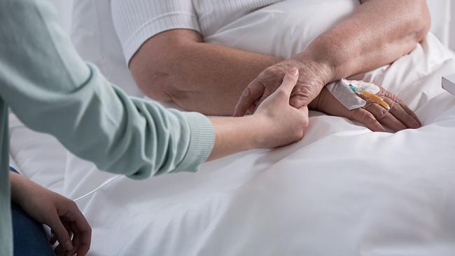Osoba trzymająca za rękę starszą osobę leżącą w łóżku