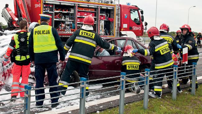 Ilustracja: Strażacy i Policjant w trakcie ćwiczenia udzielania pomocy ofiarom wypadku drogowego