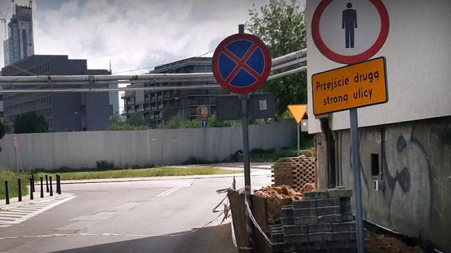 Zdjęcie z kontroli NIK: Materiały drogowe na skraju ulicy, znaki drogowe zakaz ruchu pieszych i zakaz parkowania i postoju.