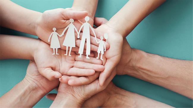 family-shaped paper cut-out being held by four pairs of hands (of adults and children)