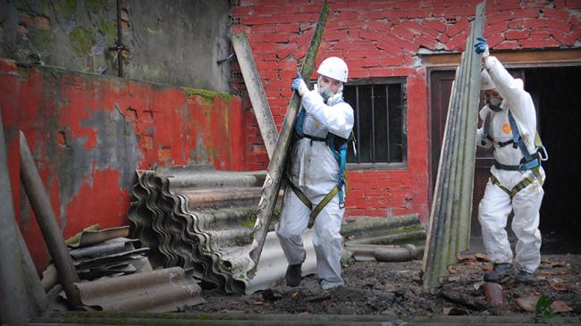 Robotnicy w kombinezonach ochronnych przenoszą płyty azbestu