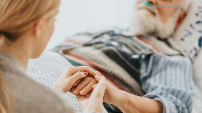 Kobieta trzyma za rękę starszego mężczyznę z drenem tlenowym