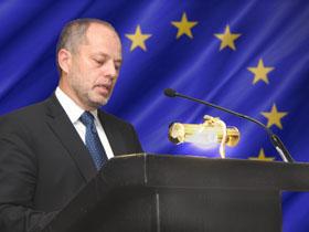 Prezes NIK Jacek Jezierski przemawia na mównicy w tle flaga Unii Europejskiej