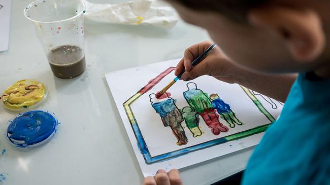 Dziecko koloruje farbami rysunek rodziny