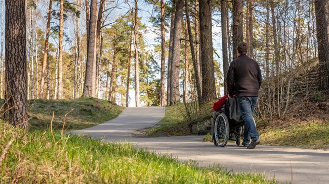 Opiekun spaceruje z osobą na wózku po parkowej ścieżce