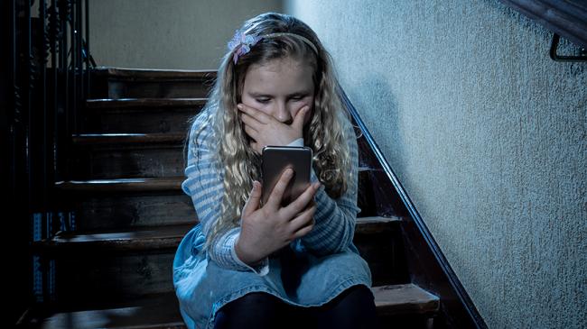Dziecko siedzące na schodach korzysta ze smartfona. Zdjęcie ilustruje zagadnienia bezpieczeństwa dzieci w internecie i korzystania z urządzeń mobilnych.