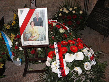 Portret Lecha i Marii Kaczyńskich wśród wieńców złożonych przy ich grobie