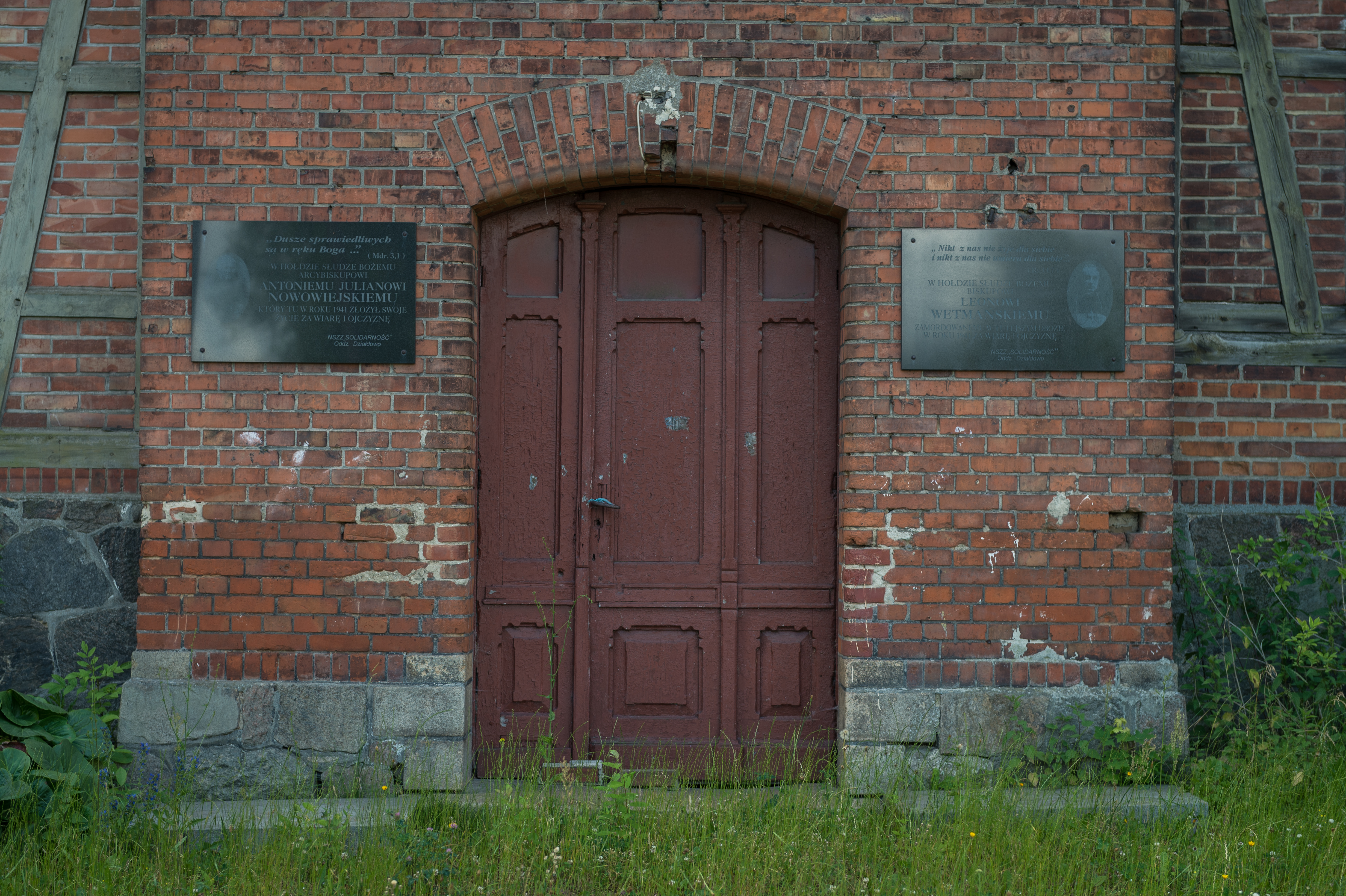 Main entrance to the building with two memorials on both sides, commemorating two bishops Nowowiejski and Wetmański who were killed in the concentration camp in Działdowo
