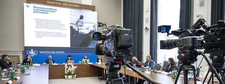 Kamery stacji telewizyjnych rejestrujących panel, w tle uczestnicy i jeden ze slajdów przedstawianej z prezentacji